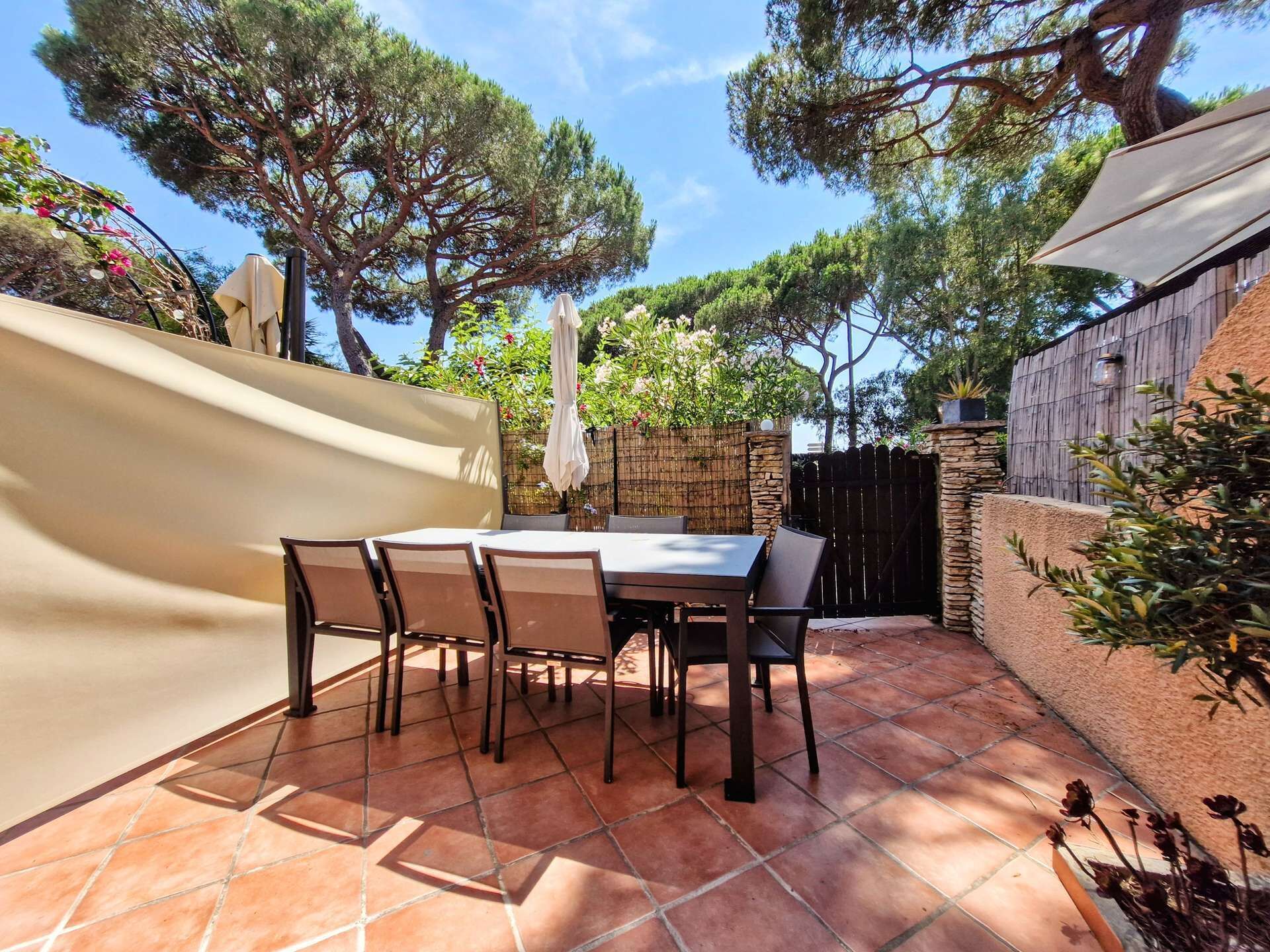 Een terras met een tafel en stoelen, omgeven door een stenen muur en bomen.