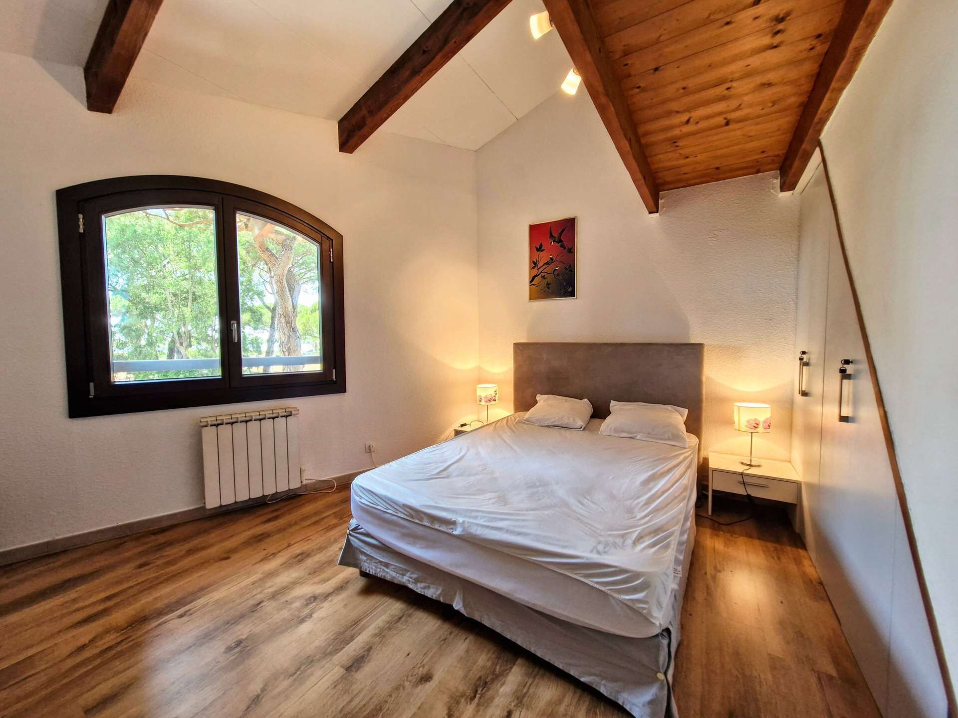 A bedroom with a bed, a window, a radiator, and a painting on the wall.
