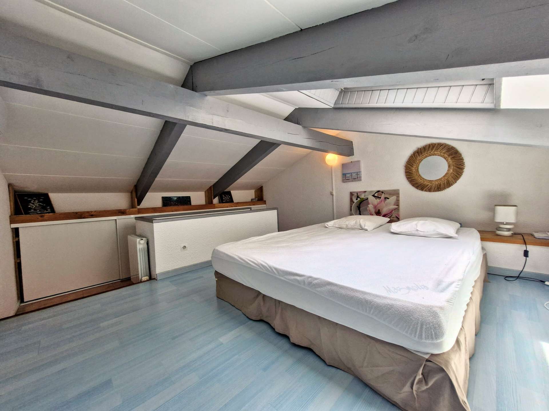 Ein Schlafzimmer mit einem Bett, einem Nachttisch mit Lampe, einem Wandspiegel und einer Heizung.