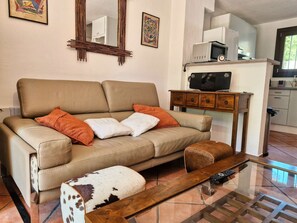 A living room with a sofa, ottoman, and a coffee table. There is a kitchen area with appliances visible. - Air-conditioned triplex flat on the Port of Hyères (HYERES)