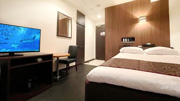 A hotel room with a bed, a desk with a television, a chair, a mirror, and a door. - Ikebukuro Grand Hotel (Tokyo)