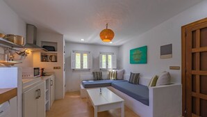 A compact living space with a kitchenette, a dining table, a sofa, and a hanging light fixture.