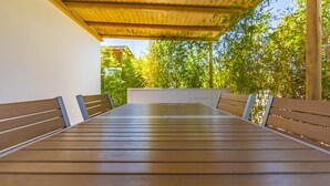 A covered outdoor seating area with a wooden table and benches, surrounded by greenery.