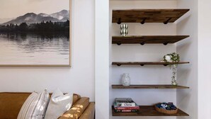 Ein Wohnzimmer mit braunem Ledersofa, einer an der Wand befestigten Holzregal mit Dekoration und einem gerahmten Landschaftsbild.