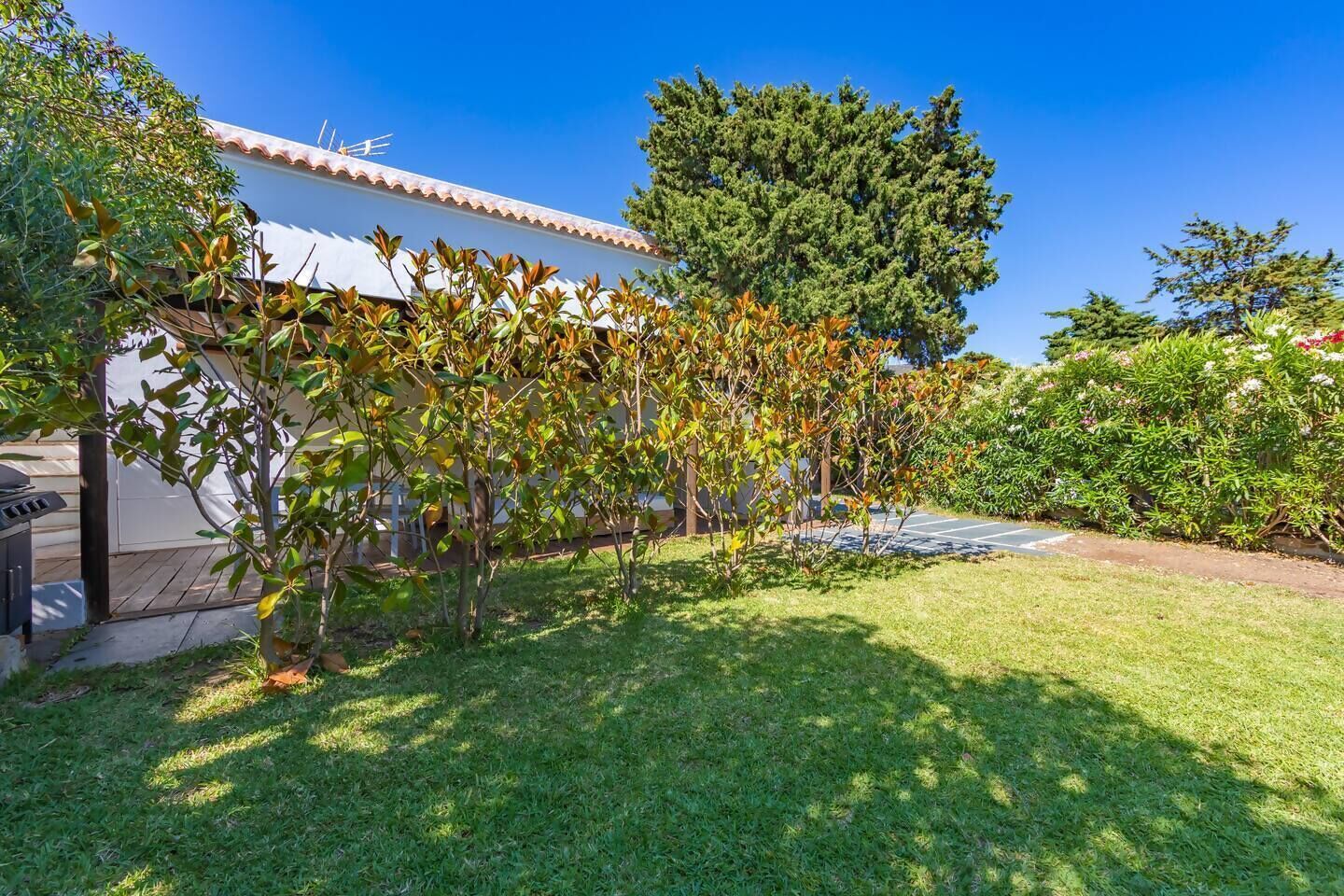 Una propiedad residencial con fachada blanca, techo de tejas y un césped bien cuidado, además de un árbol grande.