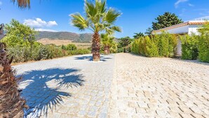 A paved pathway leading to a building with a tiled roof, surrounded by greenery and a clear sky.