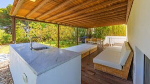 A covered outdoor area with a built-in sink, a seating area with cushions, and a barbecue grill.