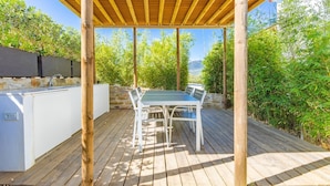 An outdoor wooden deck with a table and chairs, a stone wall, and greenery.