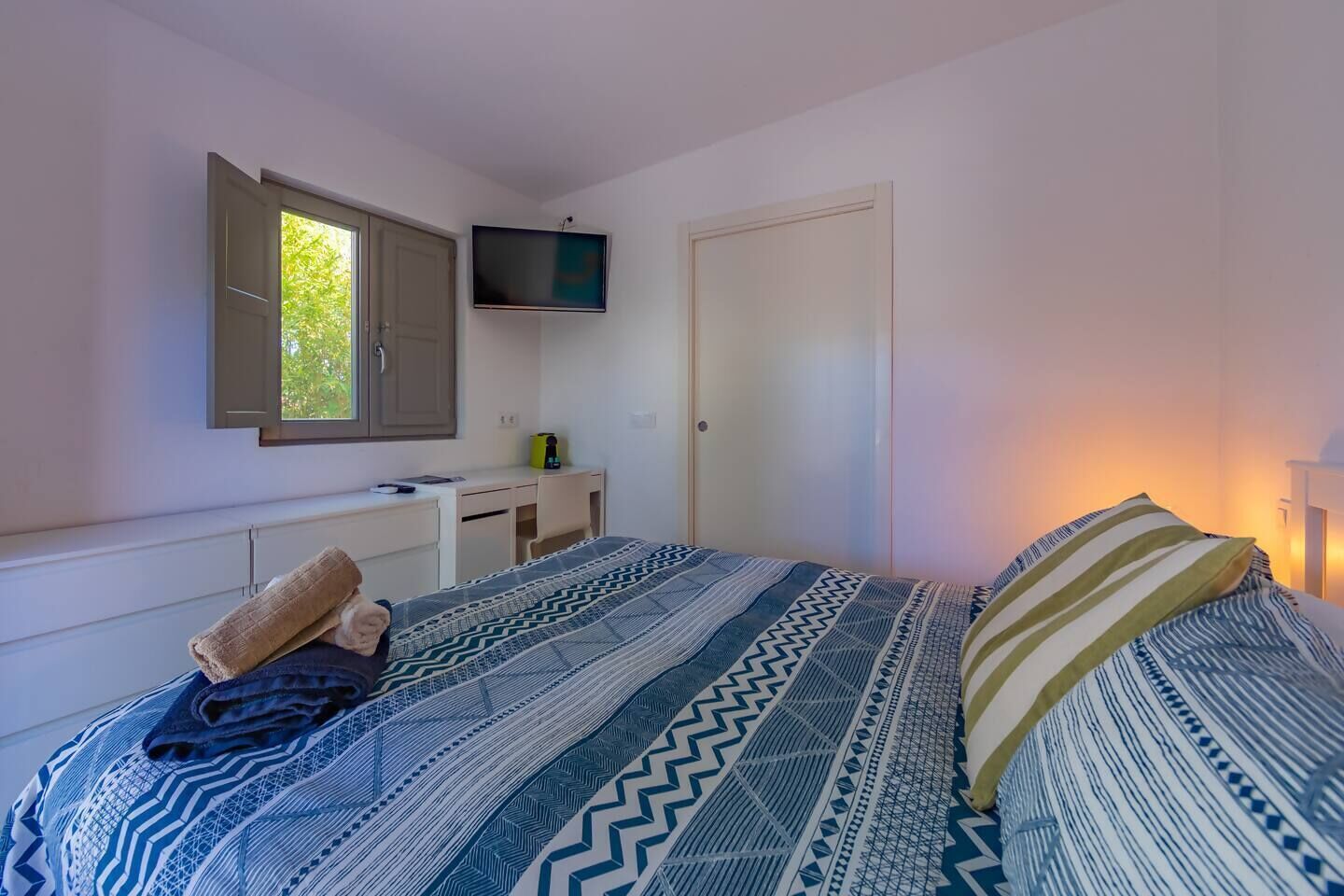 A bedroom with a bed, a desk, a television, and a wardrobe.