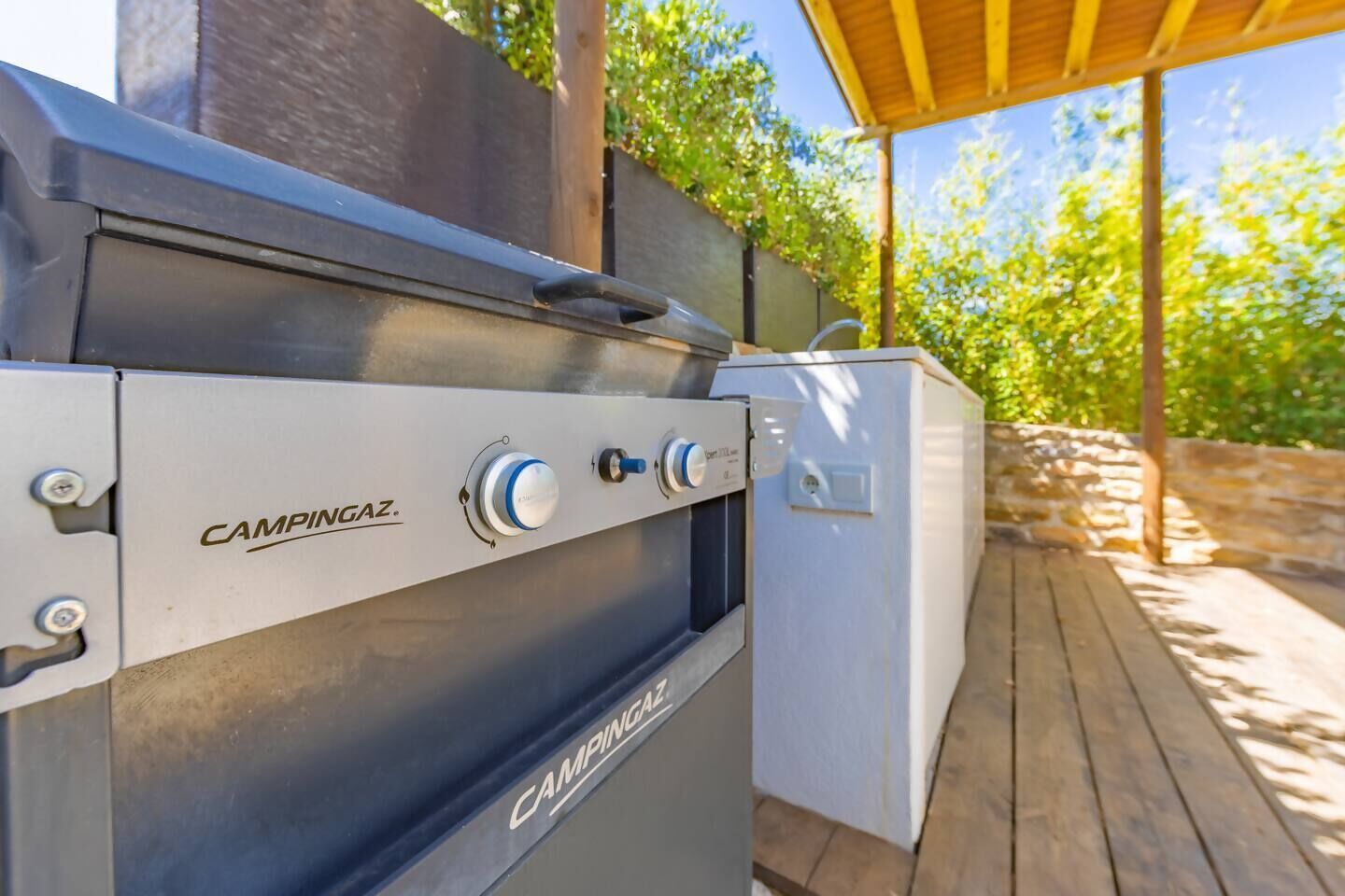 Una parrilla de camping a gas al aire libre con una terraza de madera y un muro de piedra.