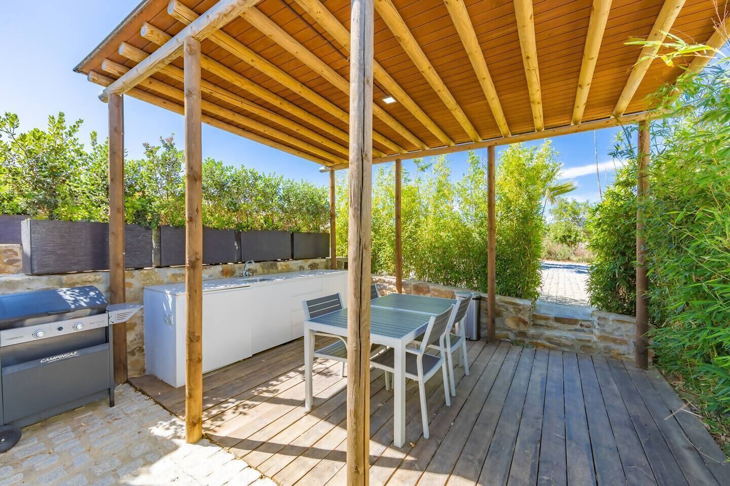 An outdoor kitchen area with a grill, sink, and dining table under a wooden pergola.