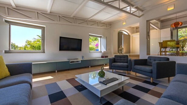 A modern living room with a flat-screen TV, sofas, a coffee table, and a large window.