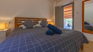 A bedroom with a bed, pillows, a nightstand, a lamp, and a mirror.
