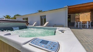 A hot tub with a control panel, lounge chairs, and a patio area with tables and chairs.