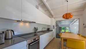 A modern kitchen with a Bosch range, a kettle, and a sink. There is a dining area with a yellow table and chairs.
