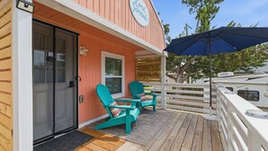 A wooden deck with two turquoise Adirondack chairs, a blue umbrella, and a white fence.
