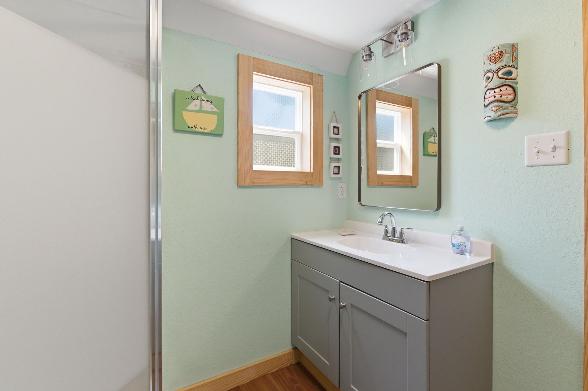 A bathroom with a window, a mirror, a sink, and a cabinet.