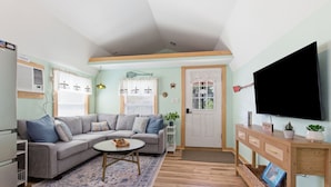 A living room with a grey sectional sofa, a round coffee table, a flat-screen TV, a wooden console table, and a door with a window.
