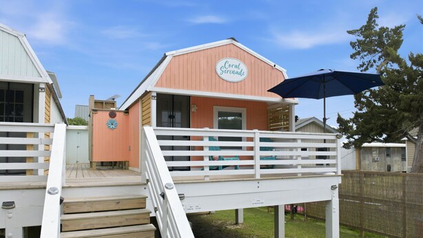 A beach house with a wooden deck, a white railing, and a sign that reads 'Coral Breeze.'