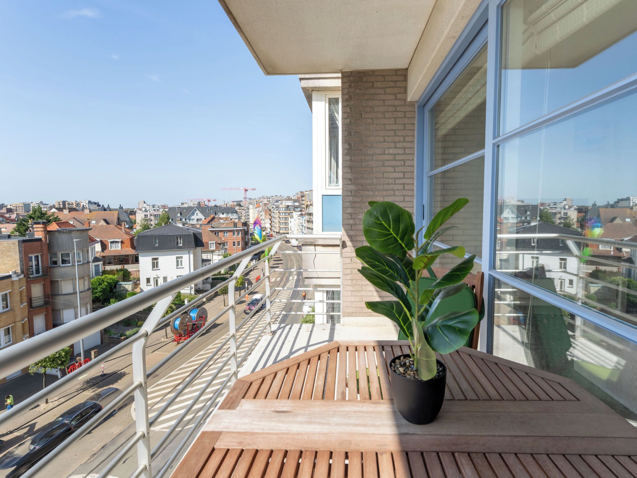 Un balcón con planta en maceta, una mesa de madera y vista a la ciudad.