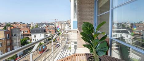 Un balcón con planta en maceta, una mesa de madera y vista a la ciudad.