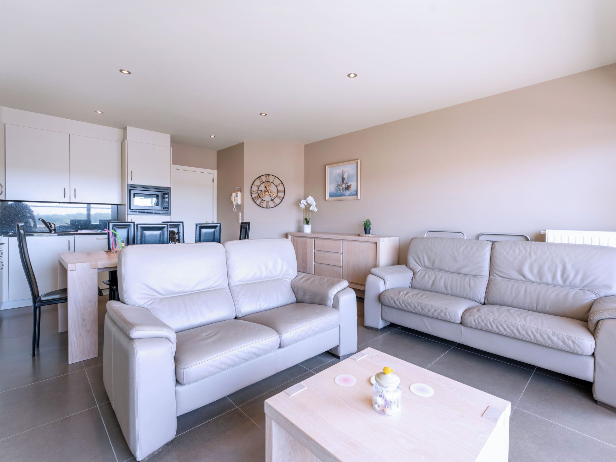 Ein modernes Wohnzimmer mit zwei Sofas, einem Couchtisch und einer Küchenzeile im Hintergrund.
