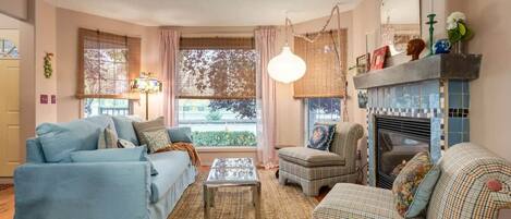A living room with a sofa, armchair, coffee table, fireplace, and large windows.