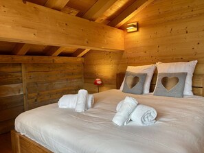 A wooden cabin-style room with a bed, pillows, and towels. - Chalet 4 Jillou - Jacuzzi  et  Alpine panorama (LA CHAPELLE D ABONDANCE)