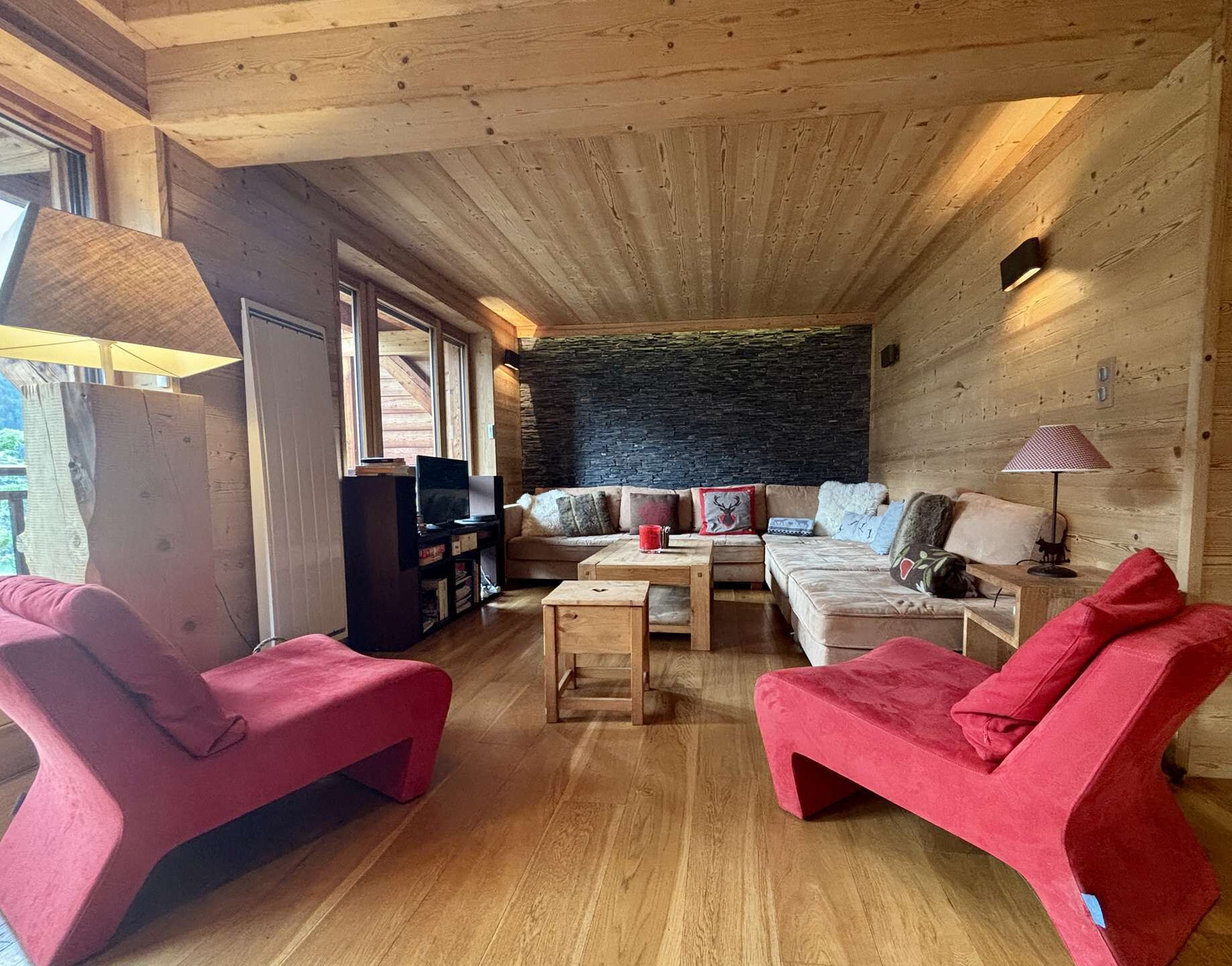 Un interior de madera acogedor con un sofá, dos sillas rojas, una mesa de centro y una pared decorativa de piedra.