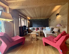 A cozy wooden interior with a sofa, two red chairs, a coffee table, and a stone accent wall. - Chalet 4 Jillou - Jacuzzi  et  Alpine panorama (LA CHAPELLE D ABONDANCE)