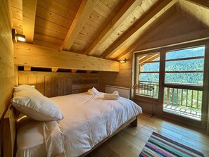 A wooden cabin bedroom with a bed, pillows, a window, and a view of the forest. - Chalet 4 Jillou - Jacuzzi  et  Alpine panorama (LA CHAPELLE D ABONDANCE)