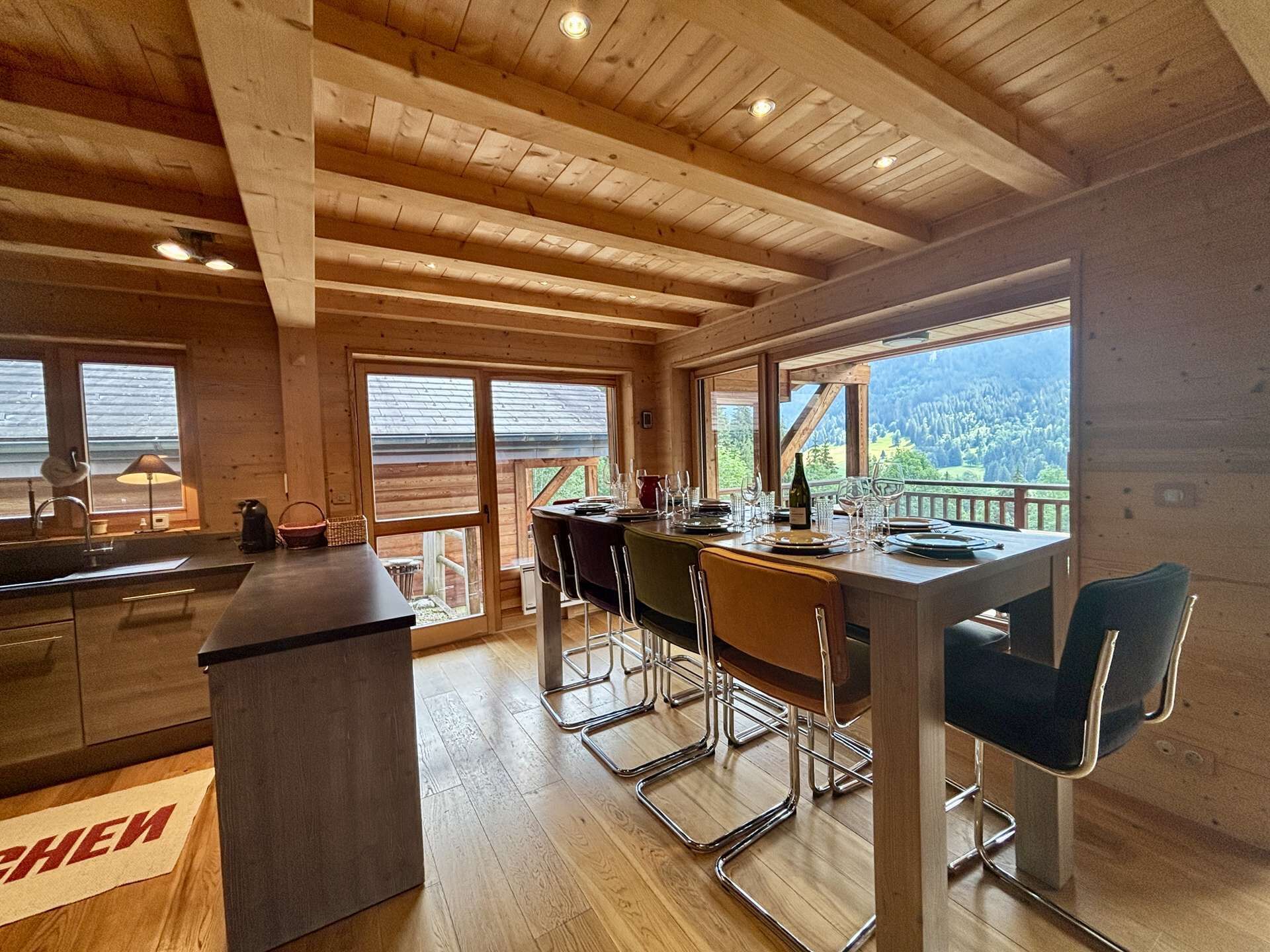 A wooden interior with a dining area, kitchen, and large windows offering a view.