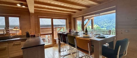 A wooden interior with a dining area, kitchen, and large windows offering a view.