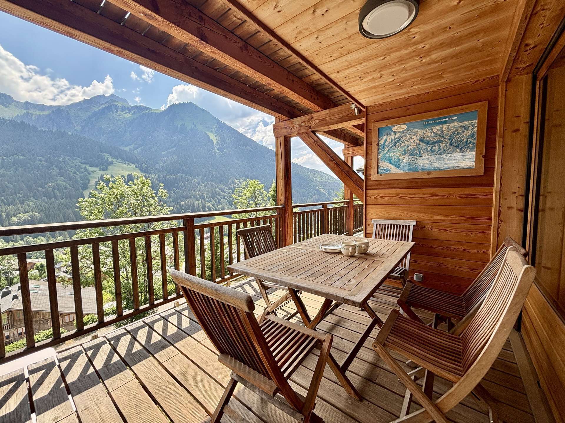Una terraza de madera con una mesa, sillas, un cuadro y vistas a montañas.