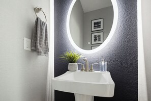 A bathroom with a white sink, a round mirror, a towel rack, and a potted plant. - Spacious 3BR, 2.5BA Home - Backyard Patio - Near Downtown Houston (Houston)