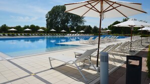 Uma piscina com espreguiçadeiras e guarda-sóis, rodeada por vegetação.