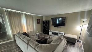 A modern living room with a sectional sofa, a flat-screen TV, a bookshelf, and a floor lamp. - Spacious & Relaxing 3-bedroom house in Fishers (Fishers)