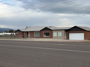 A single-story building with a garage door, a fenced area, and a road in the foreground.