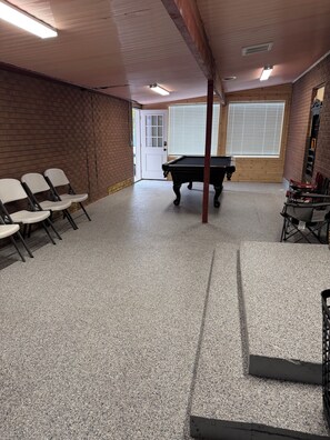 A room with a pool table, chairs, and a door leading outside.