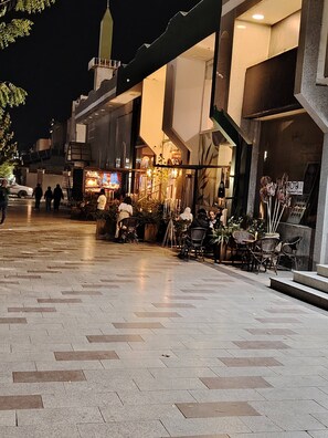 An outdoor seating area with tables and chairs, a small kiosk, and a mosque in the background. - Khair Jewaar Big Ground Apart (Madinah)