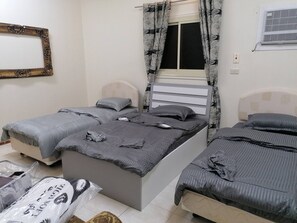 A bedroom with two beds, a window with curtains, a radiator, and a wall-mounted mirror. - Khair Jewaar Big Ground Apart (Madinah)