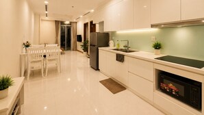 Una cocina moderna con armarios blancos, un microondas integrado y un comedor con una mesa y sillas blancas.
