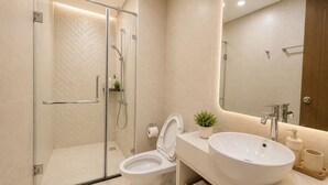 Un baño moderno con cabina de ducha de vidrio, inodoro blanco, lavabo amplio y espejo.