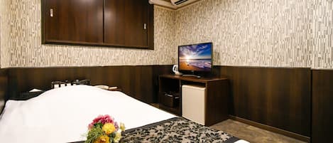 A hotel room with a bed, a television, a small desk, and a wall-mounted air conditioner.