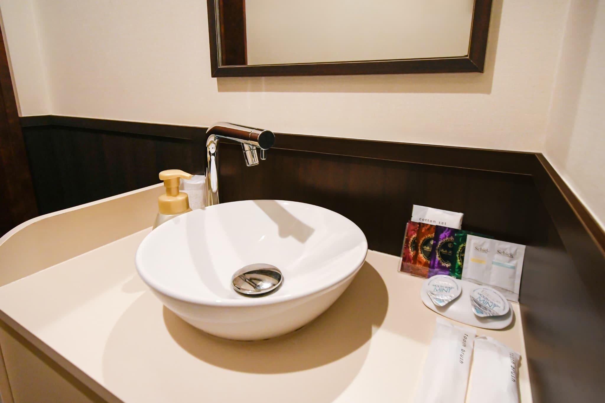 A white sink with a chrome faucet, a soap dispenser, and a mirror above it.