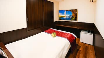 Una habitación de hotel con cama, un escritorio pequeño, un televisor montado en la pared y un cuadro.