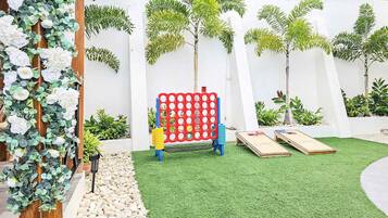 Un patio con césped artificial, un juego de mesa colorido y diversas plantas.