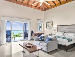 Une pièce spacieuse comprenant un grand lit, un canapé, une table basse en bois et un balcon avec vue sur l’océan.