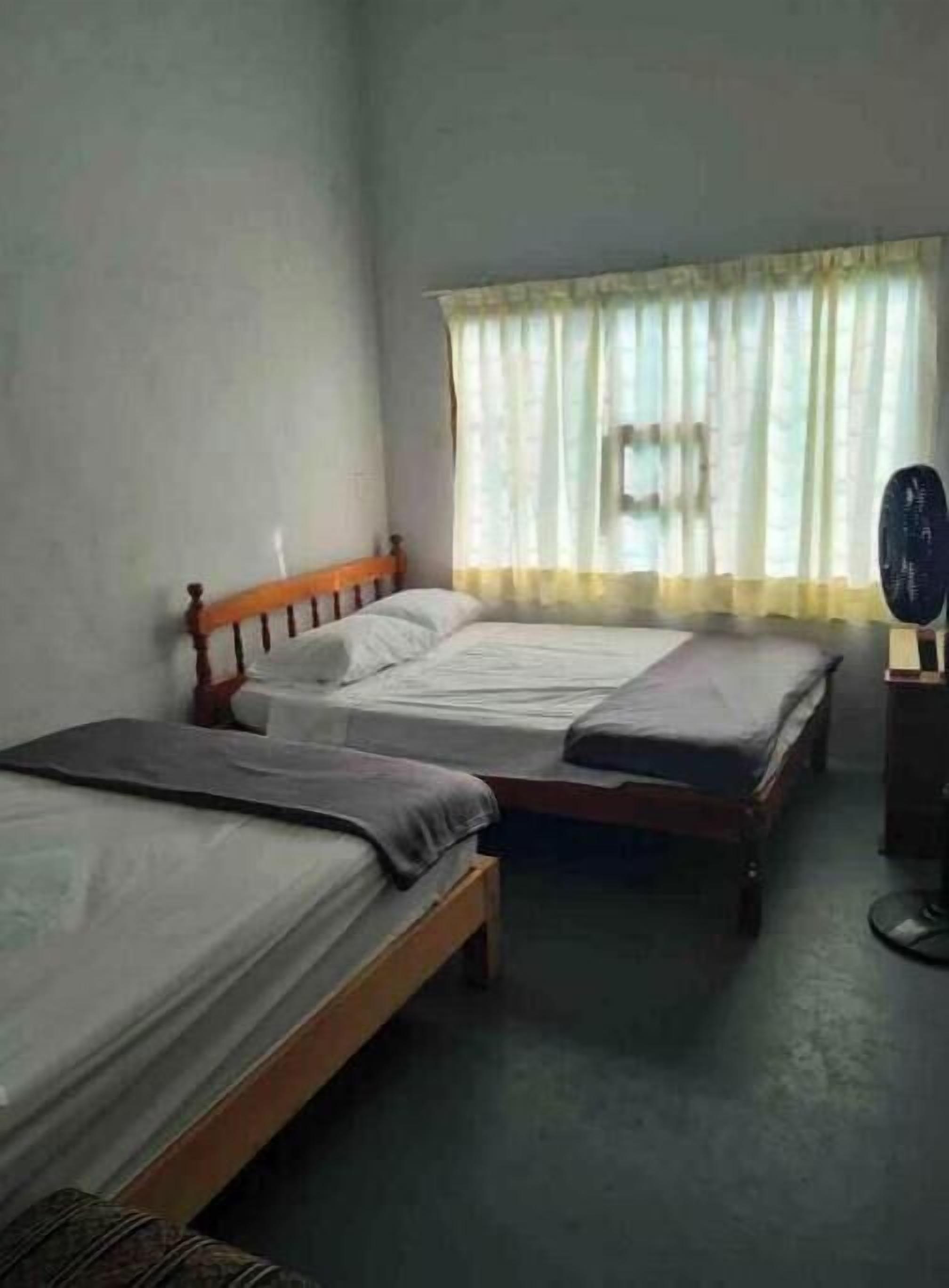 Een kamer met twee eenpersoonsbedden, een raam met gordijnen, een klein tafeltje en een stoel.
