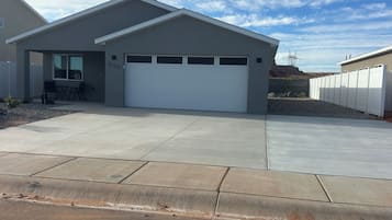 Une maison moderne de plain-pied, dotée d’un garage, d’une terrasse avec des chaises et offrant une vue sur un ciel dégagé.